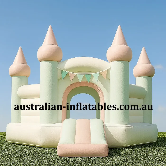 Pastel mint and peach inflatable jumping castle with castle turrets, front slide entrance and soft boutique styling displayed outdoors on grass.